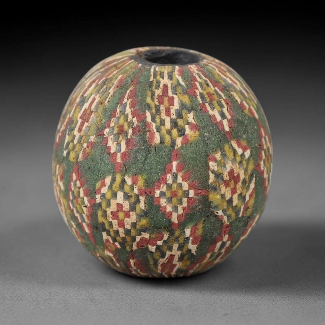 Ancient Glass Mosaic Bead - Roman Bead, 40ZM: This ancient bead is crafted from polychrome mosaic glass, formed using the millefiori technique characteristic of Roman glassworking traditions. The spherical form features a repeating geometric patt