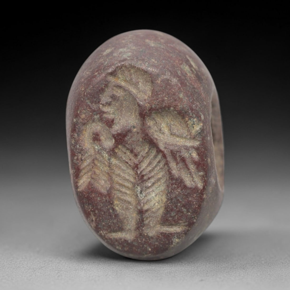 Ancient Stone Hemispherical Stamp Seal - Near Eastern Anthropomorphic Figure, 94ZS: Crafted from dense, reddish-brown stone, this hemispherical stamp seal bears incised carving of a stylized anthropomorphic figure, depicted with a distinct headdress, defined facial profile, and segme
