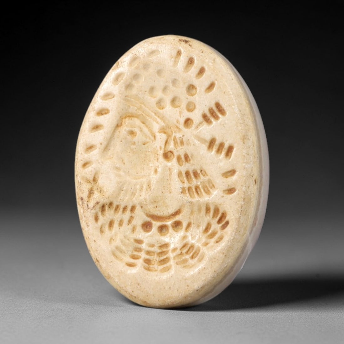 Ancient Stone Royal Bust Intaglio - Near Eastern Amulet, 38AR: This oval intaglio is carved from a pale, creamy stone matrix, featuring a high-relief profile depiction of a royal or divine figure, adorned with an elaborate beaded headdress and incised linear deta