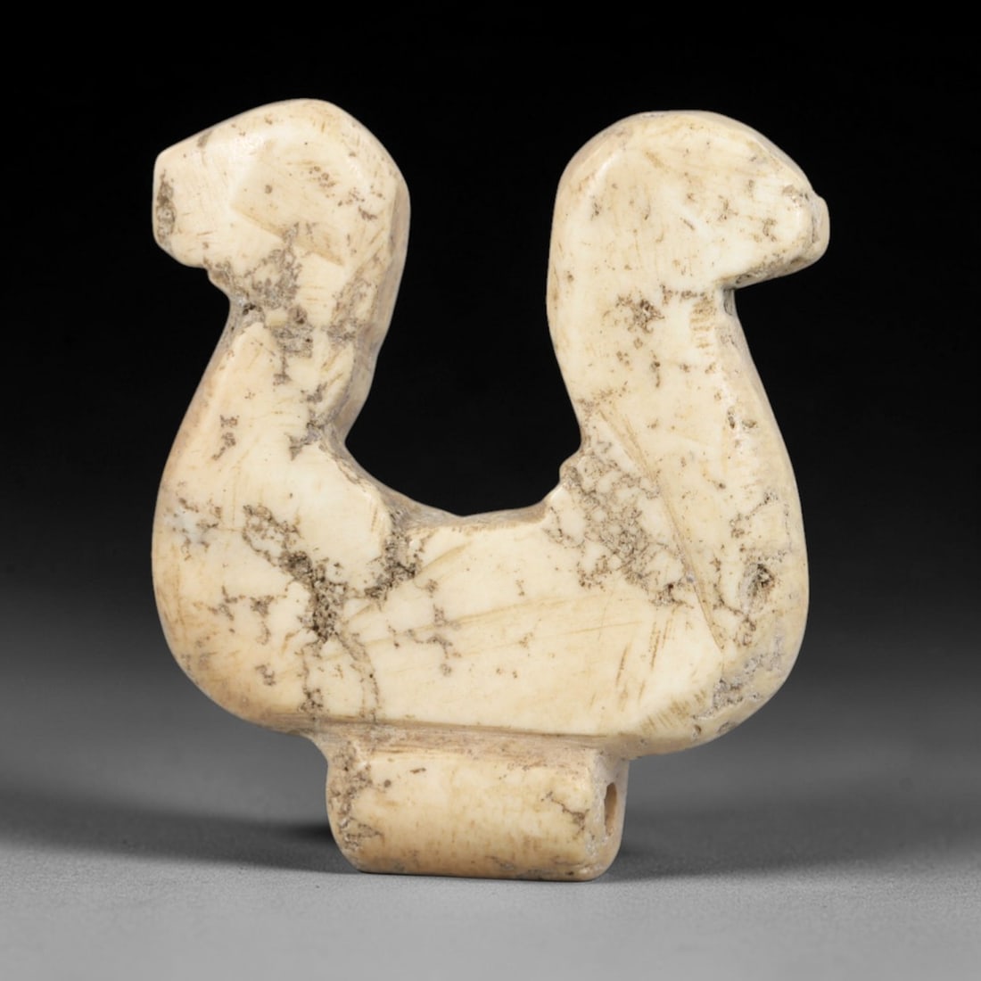 Ancient Stone Double Bird Head Amulet - Near Eastern Ritual Figure, 88AR: Carved from pale, weathered stone, this amulet features a symmetrical U-shaped form with two stylized bird heads facing opposite directions, mounted on a rectangular pierced base for suspension. Incis