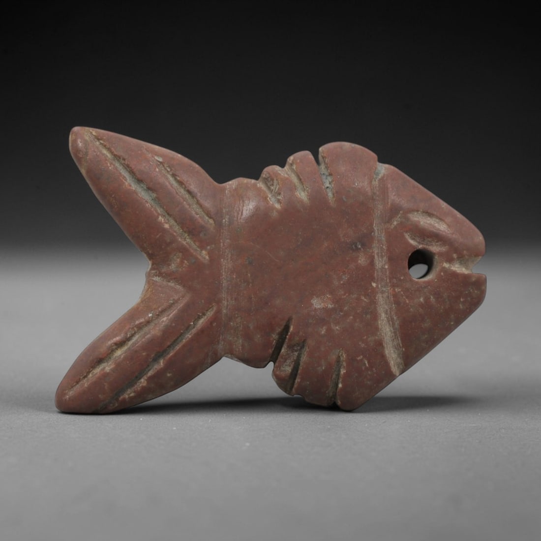 Ancient Egyptian Stone Fish Amulet - Carved Pendant Figure, 60ZV: This amulet is carved from a rich, reddish-brown siltstone, with incised linear details defining its stylized fish form. The piece features a distinct head with a suspension hole for wearable use, inc