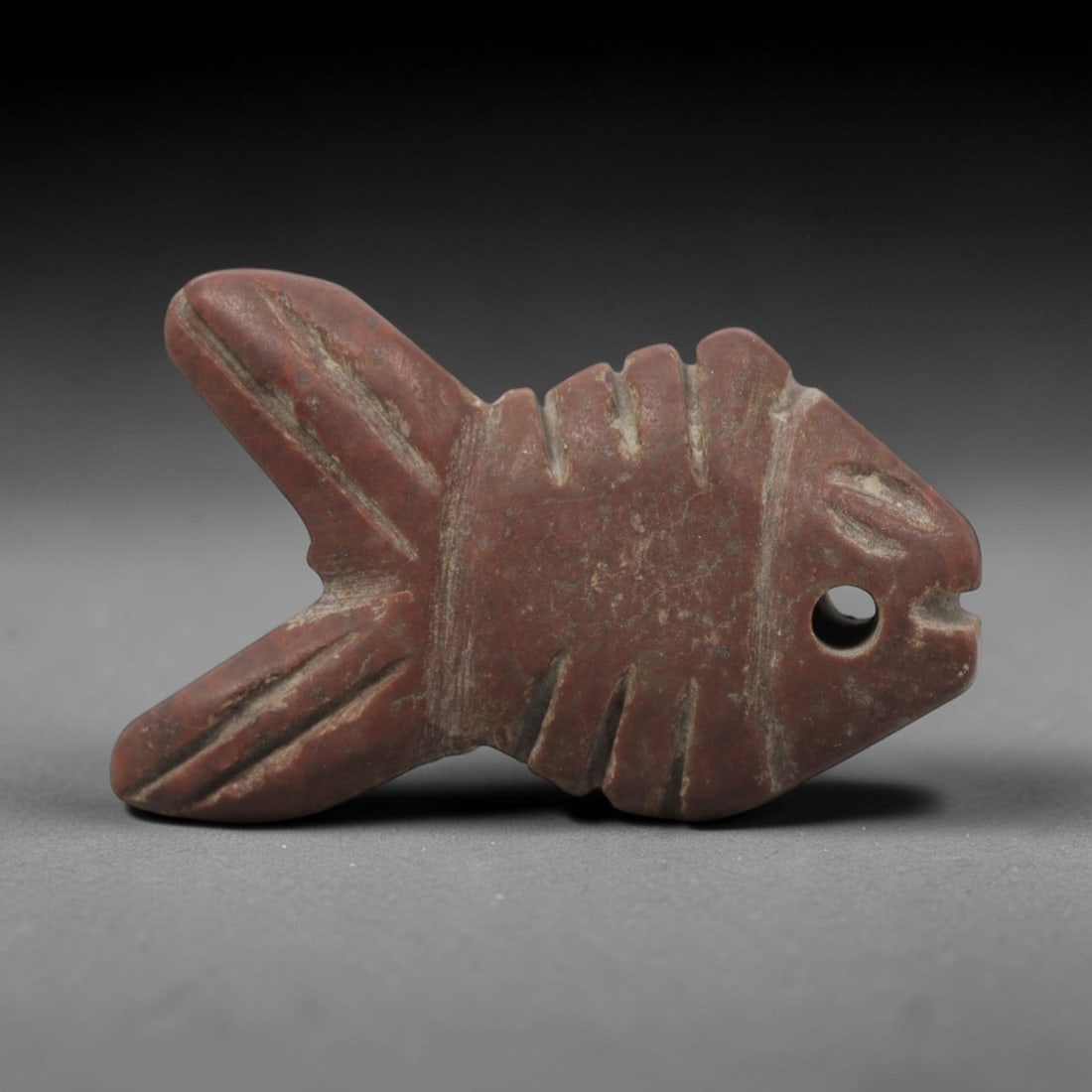 Ancient Egyptian Red Stone Fish Amulet - Carved Pendant Figure, 27ZV: This amulet is carved from a rich, deep red stone with natural mineral speckling, likely brecciated jasper or red steatite, featuring a stylized fish form. The piece displays a streamlined body with i