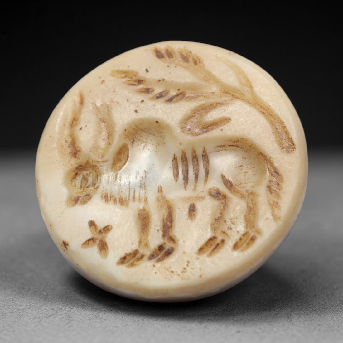 Ancient Agate Intaglio Bead - Near Eastern Ibex Motif, 25ZW: Carved from pale banded agate, this circular intaglio bead features a recessed depiction of a standing ibex with curved horns, accompanied by a stylized vegetal branch and star-like geometric detail,