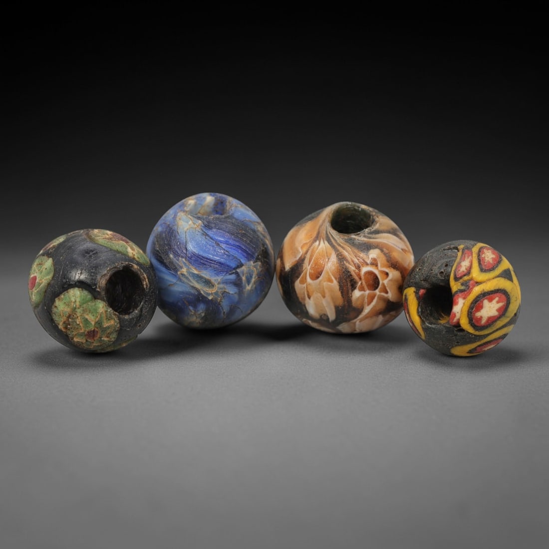 A Group of Venetian Mosaic and Swirl Glass Beads, 19th-20th Century, 91ZM: Fabricated from opaque and translucent glass, the group consists of four spherical beads with central perforations for suspension. One bead is formed with a black base and embedded green and red mosai