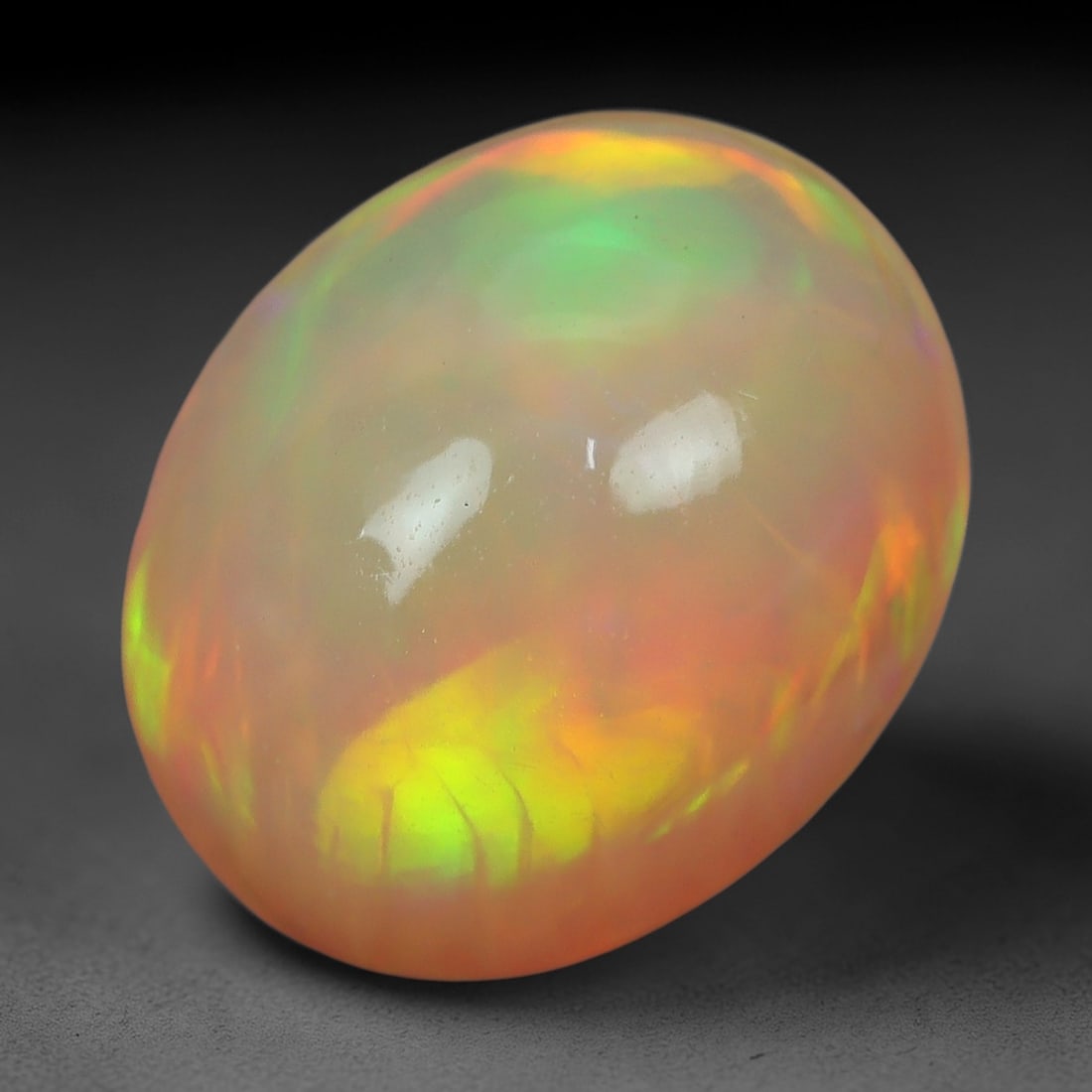 2.42 Carats Sunset Flash Ethiopian Welo Opal - Natural Loose Gemstone, 85XN: This stunning Ethiopian Welo opal, weighing 2.42 carats and cut into a smooth oval cabochon measuring 10.6 x 8.8 x 5.1 mm, radiates a warm, sunset-inspired play-of-color. Rich bands of tangerine orang