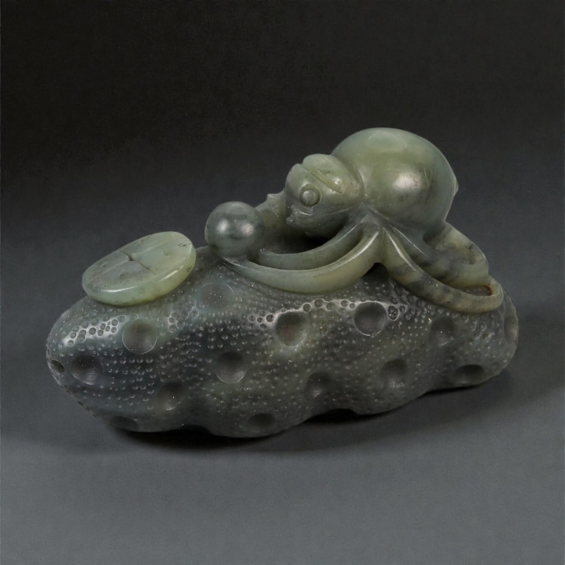 A Chinese Nephrite Jade Spider Carving, 20th Century, 77FB: Carved from dark green nephrite jade with mottled inclusions and areas of lighter translucency, the object is modeled as a spider resting upon a textured ground. The spider is carved in the round, wit