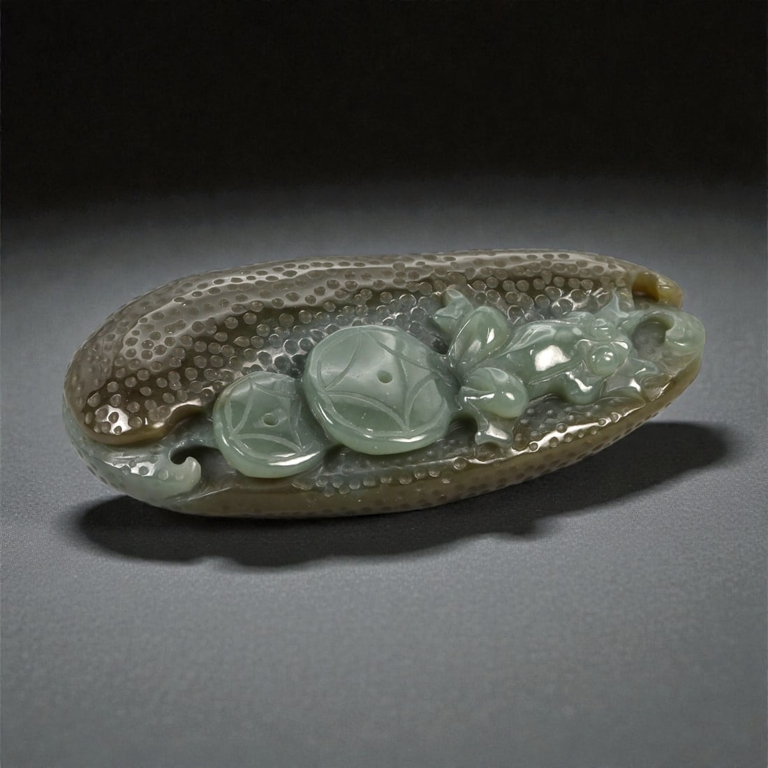 A Chinese Jade Coin and Frog Plaque, 20th Century, 76FB: Carved from mottled grey-green jade with areas of translucency and darker surface inclusions, the plaque is worked in low relief as a recumbent composition combining a frog and a group of coins set ag