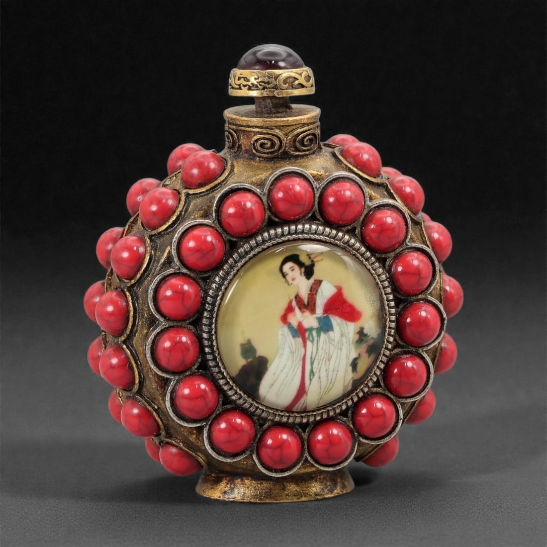A Chinese Brass and Bead-Set Snuff Bottle, 20th Century, 25FG: The bottle is constructed from cast brass with a flattened circular body raised on a short foot. The exterior is extensively embellished with applied red bead cabochons set in raised bezels, arranged 