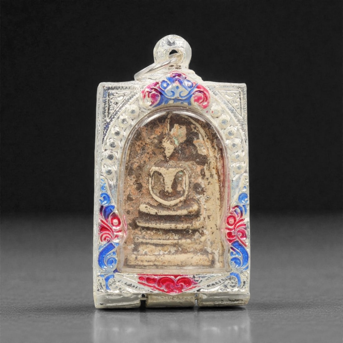 A Thai Phra Somdej Amulet Pendant, 20th Century, 90FN: This rectangular pendant features a traditional Phra Somdej core, encased in a silver frame with a transparent protective cover, measuring 5.5 x 3.5 cm (2 3/16 x 1 3/8 in.). The obverse displays the i