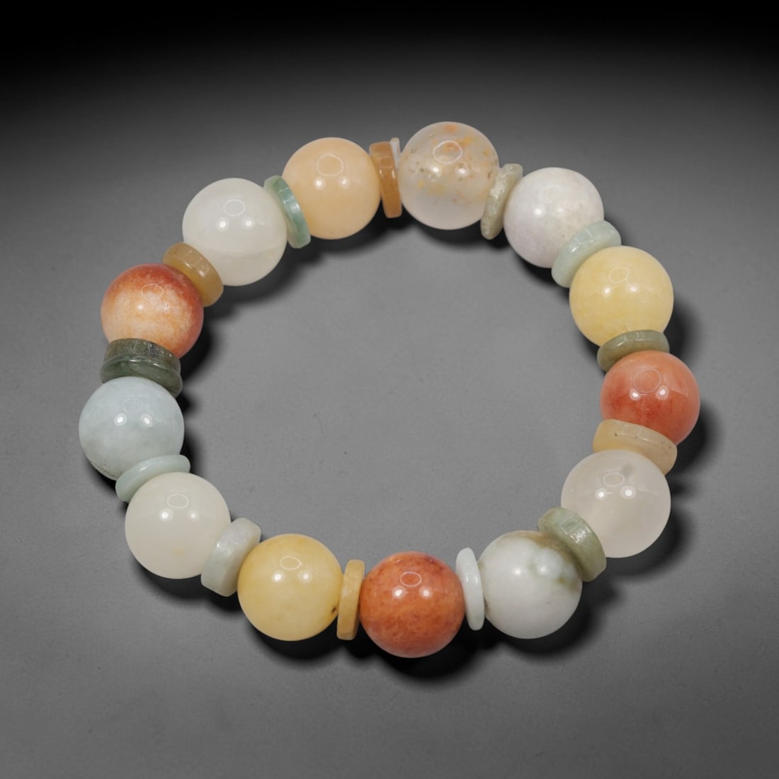 A Chinese Quartz and Jadeite Jade Bead Bracelet, 20th Century, 40ZK: Strung with spherical beads of quartz and jadeite jade, separated by flat disc-shaped spacers. The quartz beads display a range of natural hues, including white, pale yellow, orange, and reddish-orang