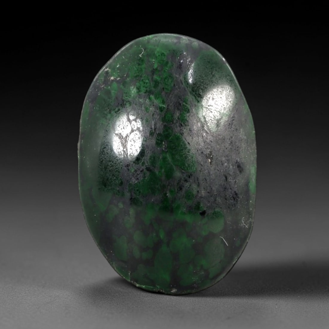9.78 Carats Dark Matrix and Green Spot Maw Sit Sit Jade Cabochon - Natural Burmese Stone, 22AB: This maw sit sit jade cabochon is fashioned into an oval, domed form with a highly polished surface. The material exhibits a dark, semi-translucent to opaque matrix, densely interspersed with distinct