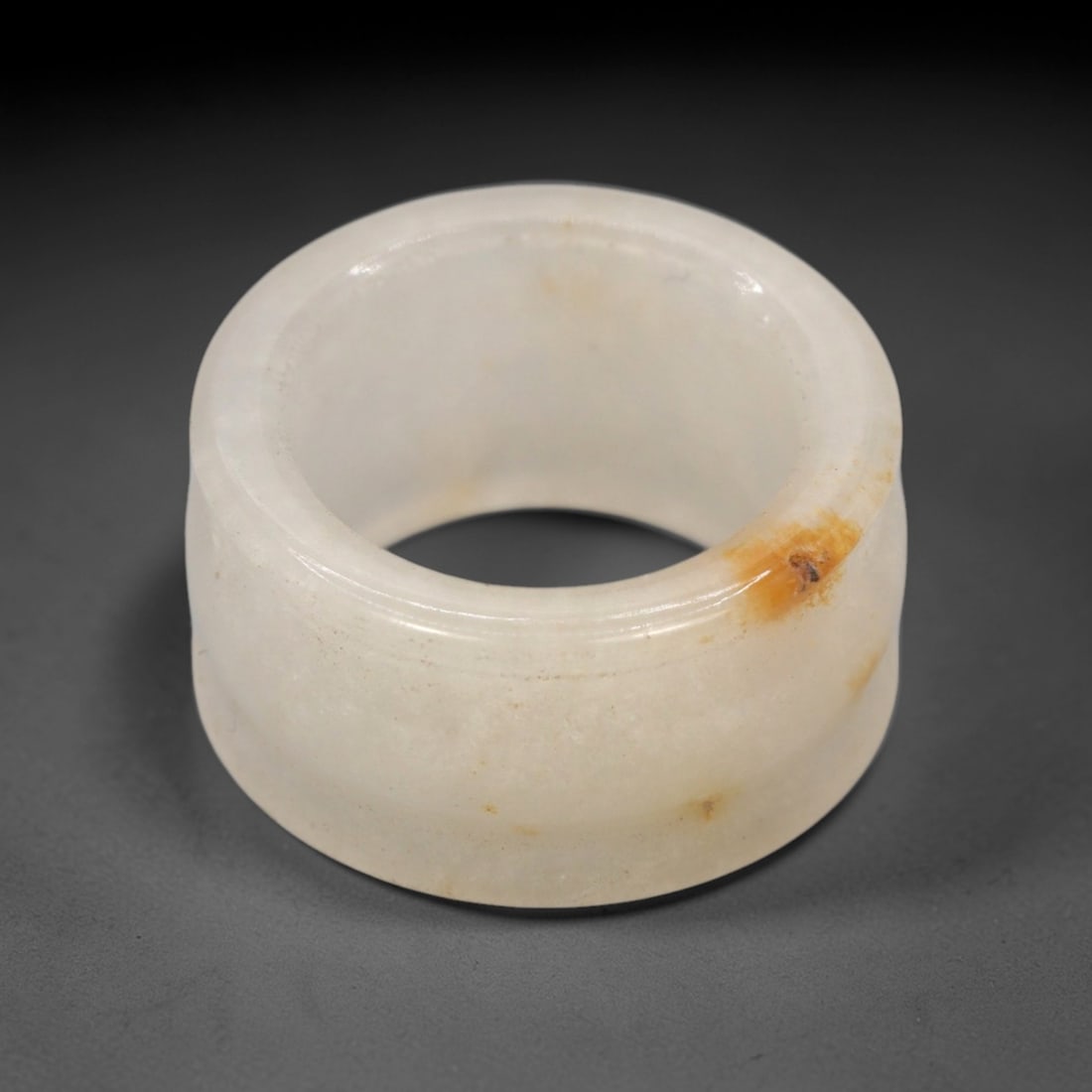 A Chinese Nephrite Jade Archer's Ring, 20th Century, 79FT: Carved from white nephrite jade with natural orange-brown inclusions and subtle tonal variation, the ring is formed as a thick, cylindrical band with a slightly flared outer profile and a concave inne