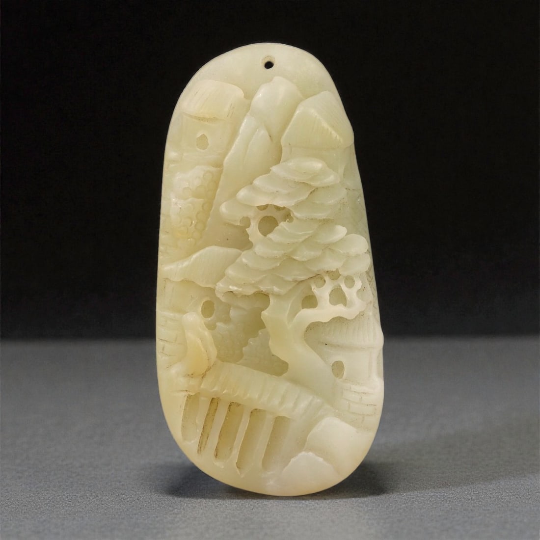 A Chinese Nephrite Jade Landscape Pendant, 20th Century, 56FA: Carved from pale cream nephrite jade with areas of soft translucency and minor natural inclusions, the pendant is worked in openwork and low relief depicting a stylized landscape composition. The surf