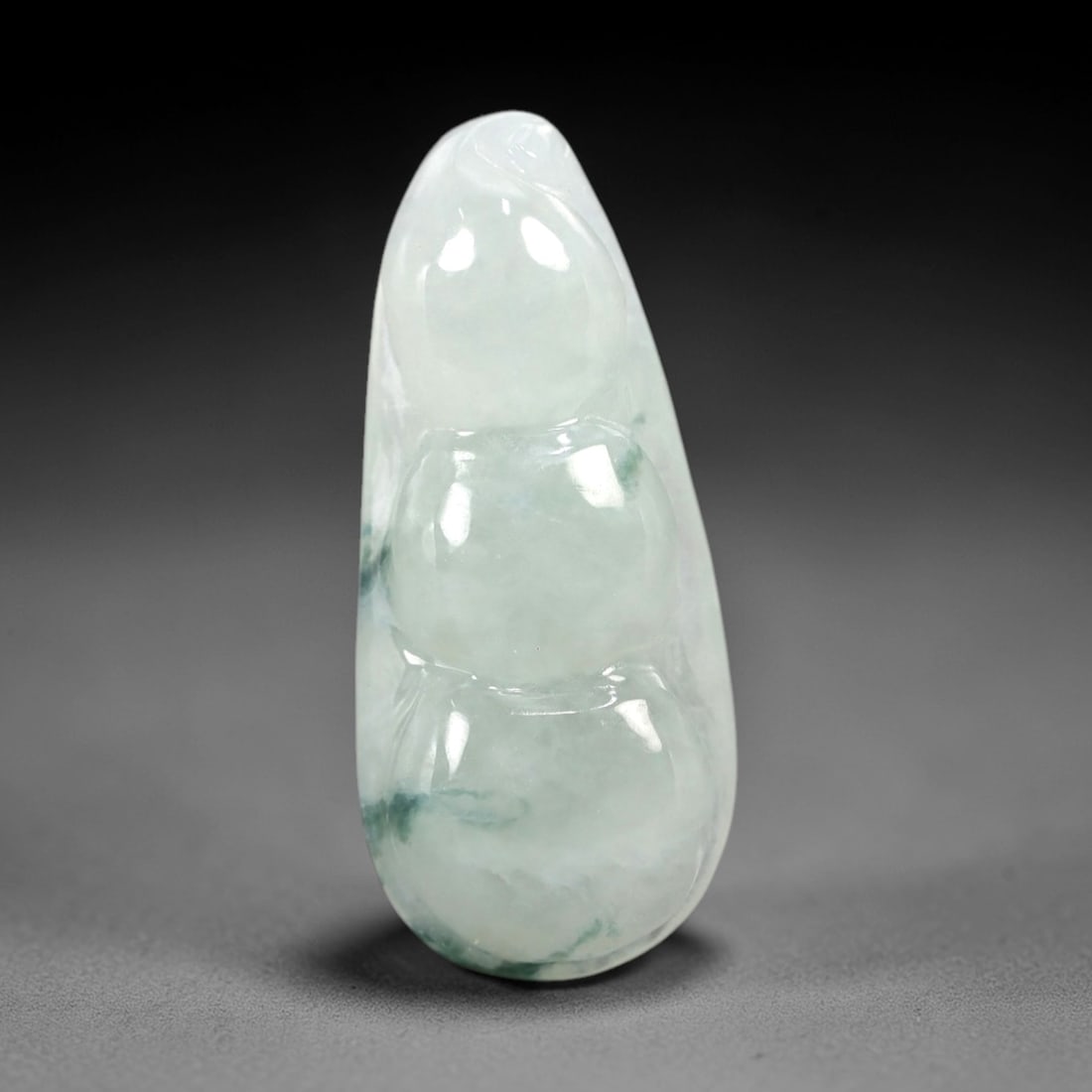 A Chinese Icy Jadeite Jade Bean Pendant, 20th Century, 51AB: Carved from translucent icy jadeite with a pale milky-white base and scattered greenish inclusions, the pendant is shaped as a stylized three-segmented bean pod. Smooth, rounded contours define each s