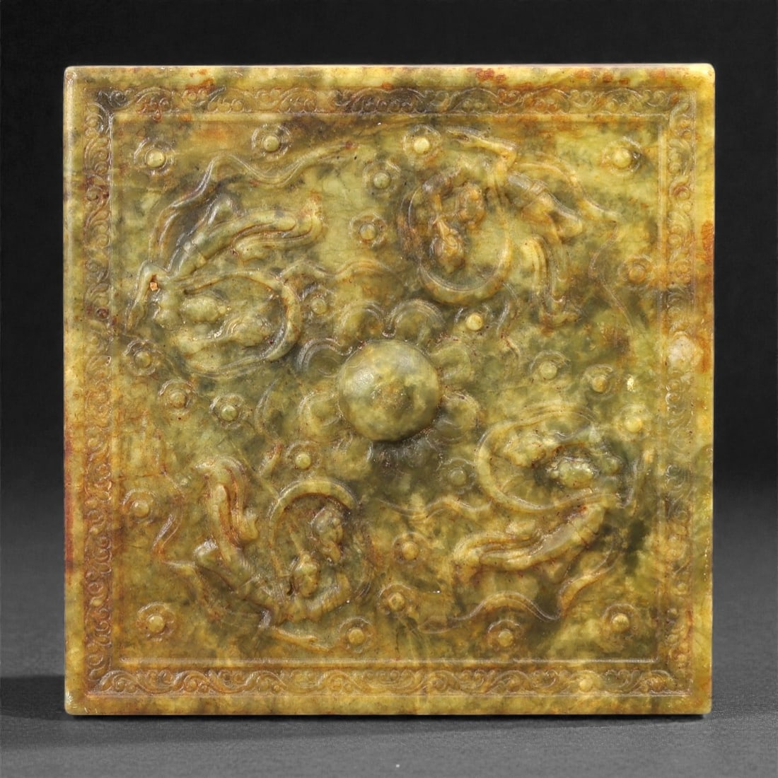 A Chinese Hetian Jade Relief Plaque, 20th Century, 89FH: Carved from mottled green and russet-toned Hetian nephrite jade, the plaque is rectangular in format with a flat reverse and a relief-carved front. The surface is worked with a central raised boss sur
