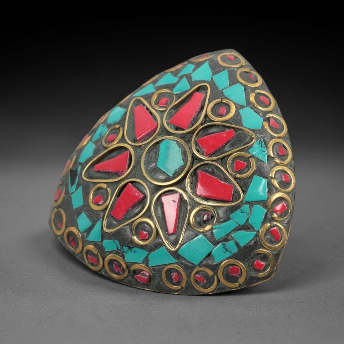 A Tibetan Gilt-Metal, Turquoise and Red Composite Stone Mosaic Ring, 20th Century, 81ZL: A bold statement ring of domed, heart-shaped silhouette, crafted in the traditional Himalayan style from a dark patinated base metal with gilt-brass alloy inlay. The entire convex surface is adorned w