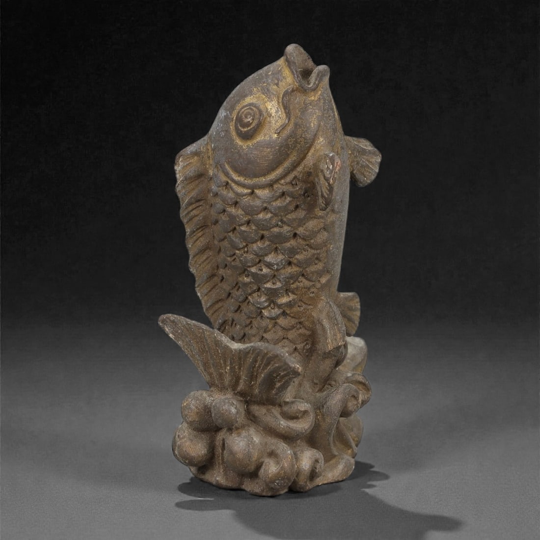 A Chinese Bronze Fish Sculpture, 20th Century, 19FH: Cast in bronze, the sculpture is formed as a single fish shown upright, emerging from stylized waves that serve as an integral base. The fish is rendered with a rounded head, prominent circular eye, a