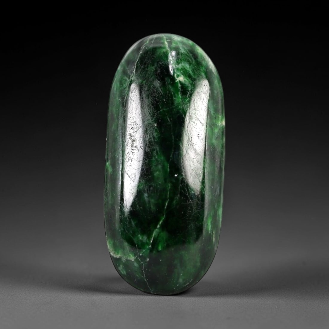 5.22 Carats Deep Green Maw Sit Sit Jade Cabochon - Natural Burmese Stone, 4AB: This maw sit sit jade cabochon is fashioned into an elongated oval form with a highly polished, domed surface. The material exhibits a deep, saturated green hue, interspersed with distinct, lighter gr