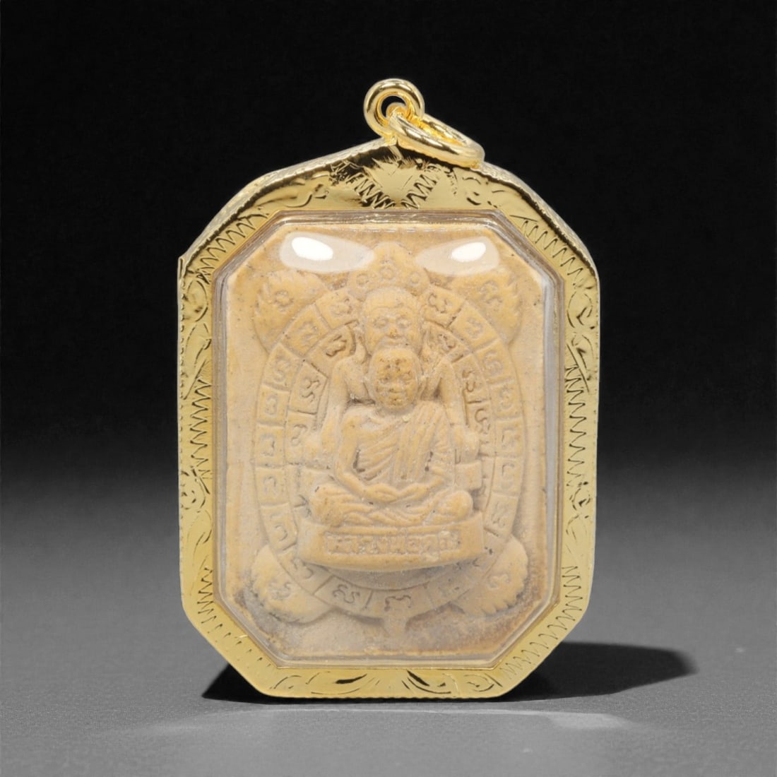 A Thai Dual-Figure Turtle Amulet Pendant, 20th Century, 26FP: This octagonal pendant features a light beige composite amulet core, encased in an ornate gilded metal frame with a transparent protective cover, measuring 5.1 x 3.4 cm (2 x 1 5/16 in.). The obverse d
