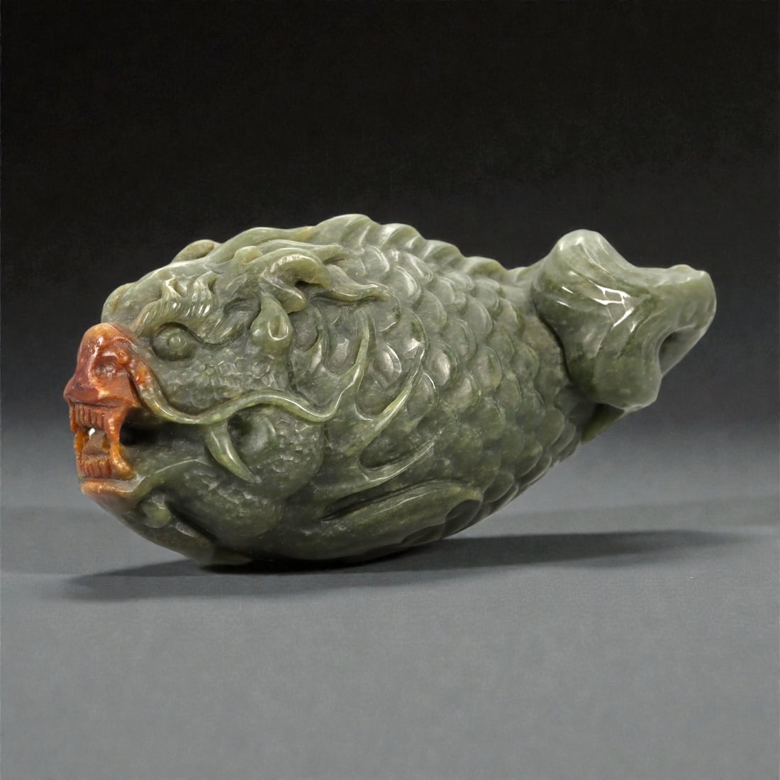 A Chinese Jade Carp-Dragon Carving, 20th Century, 22FB: Carved from a dark green jade with areas of lighter mottling and localized brown inclusions, the object is worked in the form of a hybrid creature combining a dragon head with the scaled body of a fis