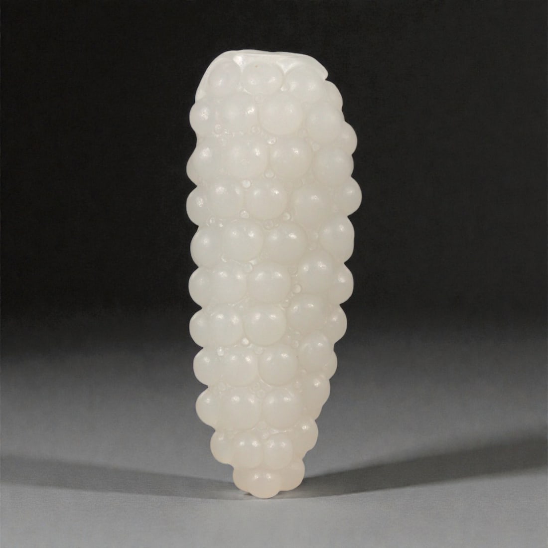 A Chinese Nephrite Jade Fruit Carving, 20th Century, 5FC: Carved from pale white nephrite jade with a high degree of translucency and subtle natural clouding, the object is modeled in the form of a clustered fruit, likely grapes, rendered as a vertical arran