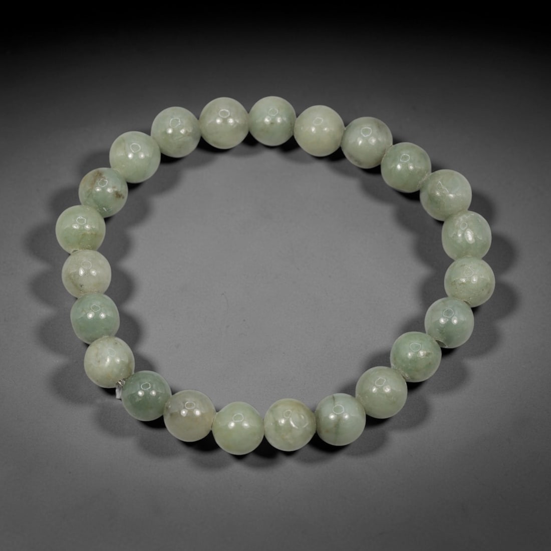 A Chinese Jadeite Jade Bead Bracelet, 20th Century, 58ZK: Composed of a single strand of spherical jadeite jade beads forming a circular bracelet. The beads display natural tonal variation from pale green to light green, with visible internal mineral inclusi