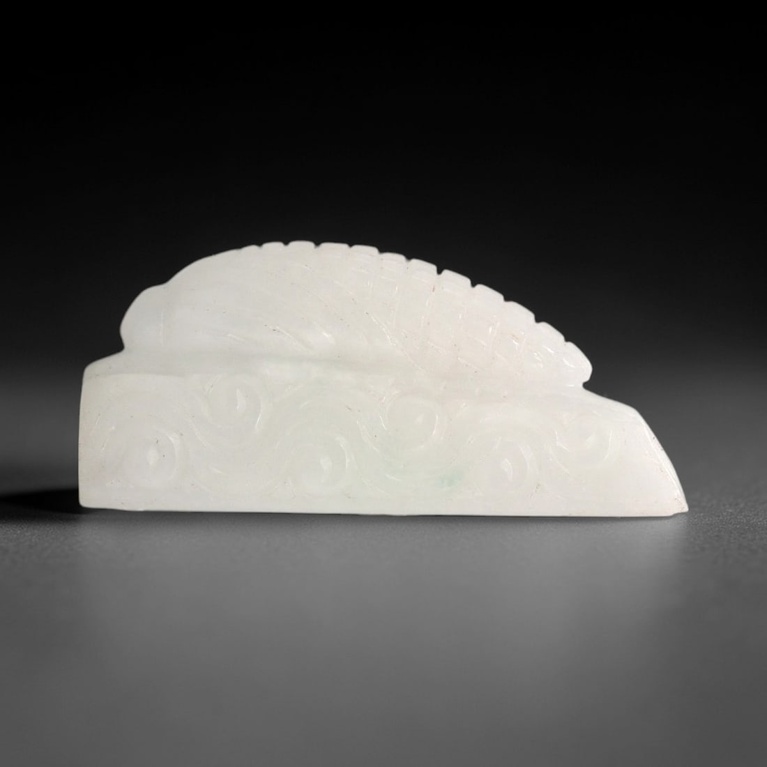 A Chinese Jadeite Jade Zoomorphic Ornament, 20th Century, 90FR: Carved from pale translucent white jadeite jade with a faint green inclusion, the ornament has a rectangular base with a raised zoomorphic figure atop. The base is decorated with continuous swirling s