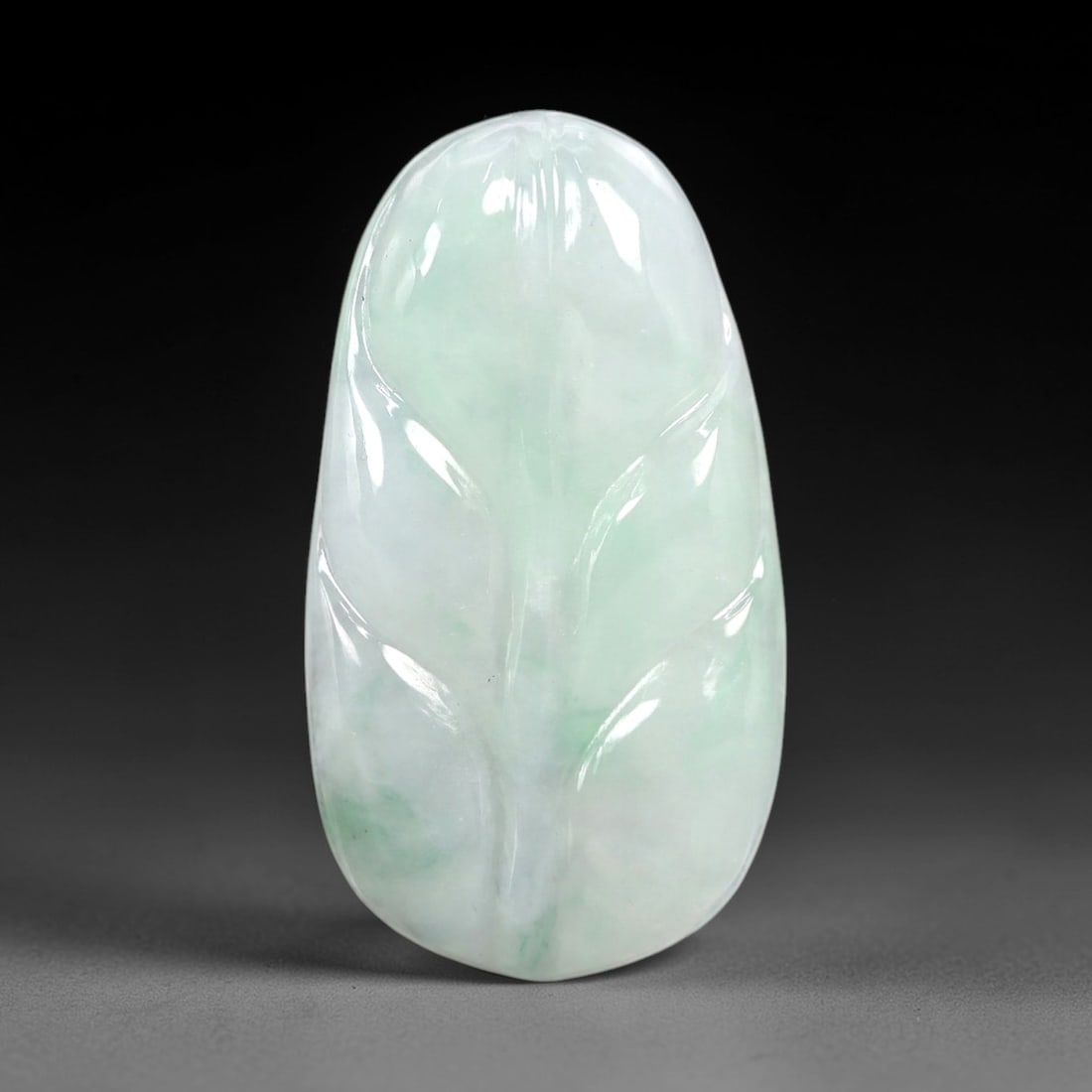 A Chinese Icy Jadeite Jade Leaf Pendant, 20th Century, 61AB: Carved from translucent icy jadeite with a pale white base and subtle greenish inclusions, the pendant is shaped as a stylized leaf with a rounded upper edge and a tapered lower tip. Incised lines def