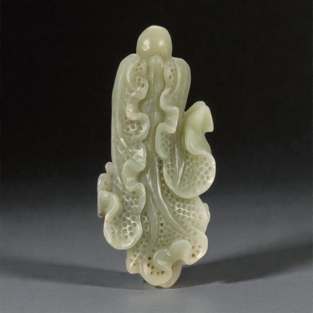 A Chinese Jade Cabbage Carving, 20th Century, 70YA: Carved from pale celadon jade with areas of light brown mineral inclusions and subtle translucency, the object is modeled as a vertically oriented cabbage with layered, overlapping leaves. The form is