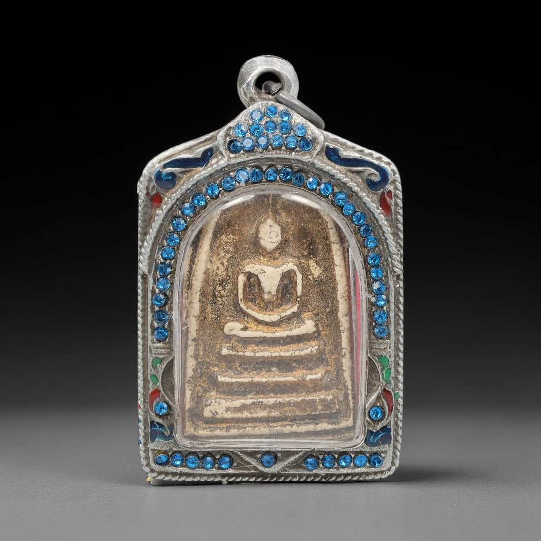 A Thai Terracotta Buddha Amulet in Metal Case, 20th Century, 67ZH: The amulet is formed from terracotta, with a tan matrix containing visible particulate inclusions and surface patination. The obverse bears a molded relief of a seated Buddha in meditative posture on
