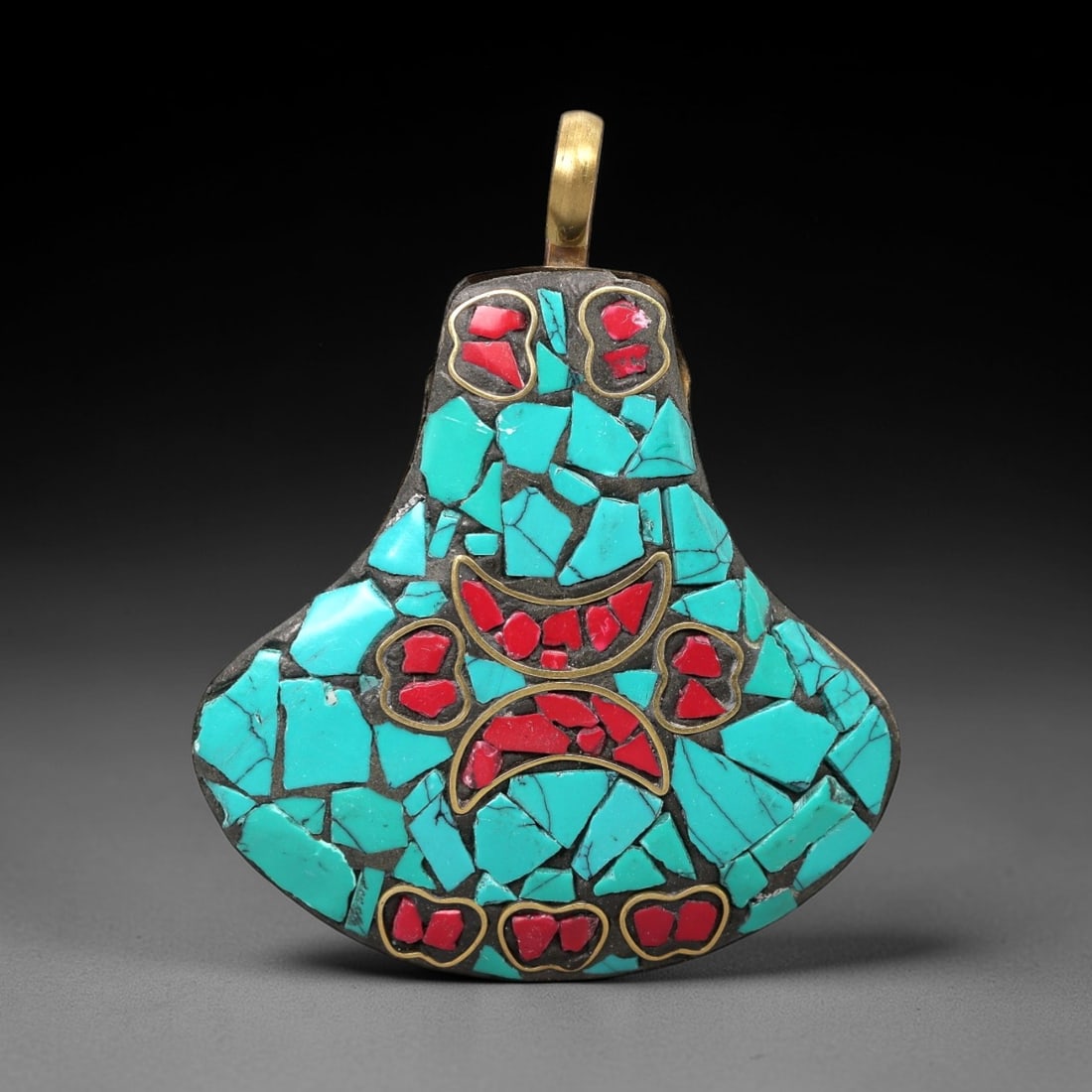 A Tibetan Brass Pendant with Turquoise and Coral Inlay, 20th Century, 92XM: Crafted from brass with a dark patinated base, the pendant is inlaid with irregular fragments of turquoise and coral, set within a black matrix. The form is a stylized, flattened gourd shape, tapering