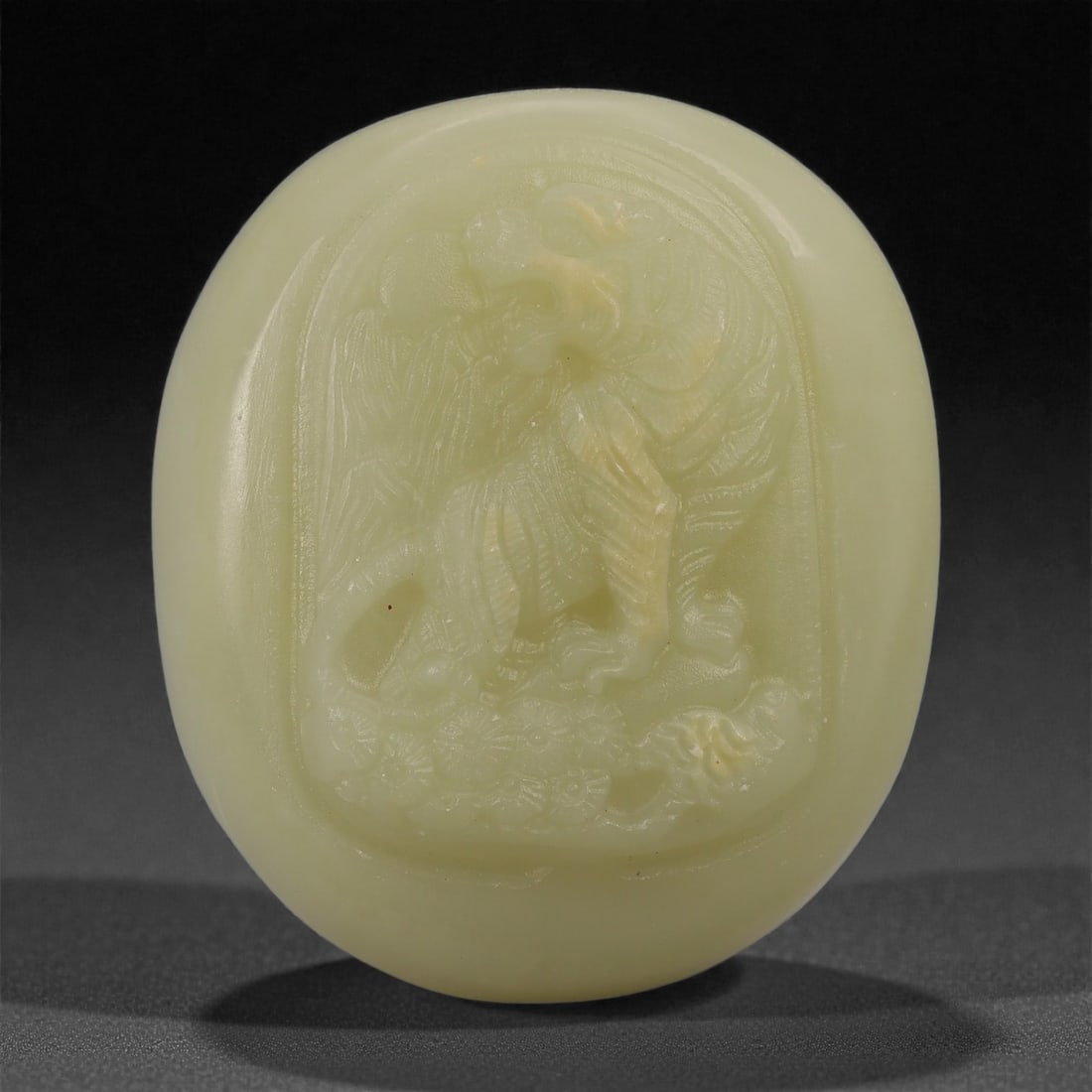 A Chinese Hetian Nephrite Jade Pebble Carving of a Tiger, 20th Century, 70FD: Carved from a naturally rounded Hetian nephrite jade pebble of pale celadon tone with soft translucency. The pebble is worked in shallow relief on one face with the image of a crouching tiger, its hea