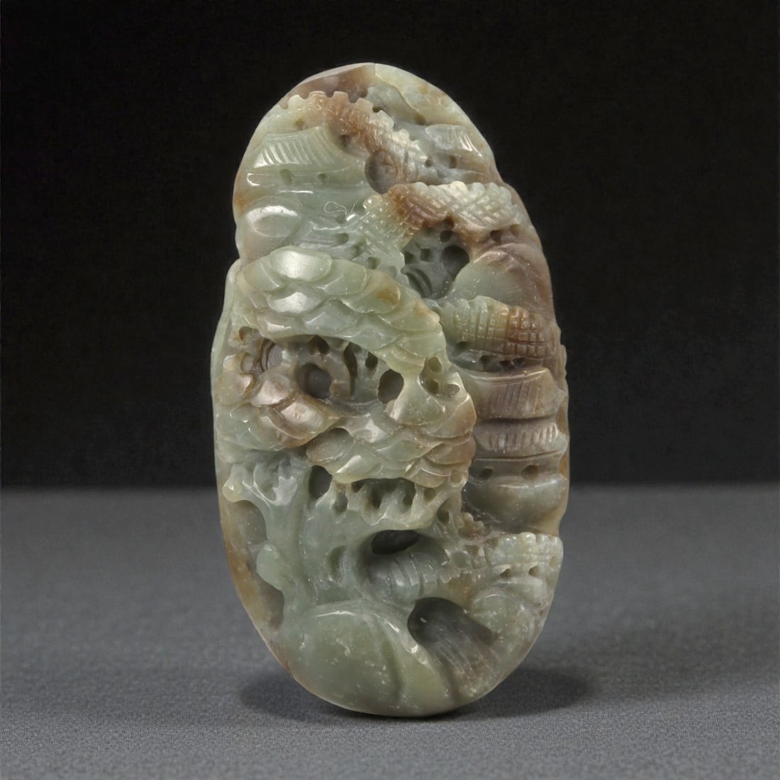A Chinese Nephrite Jade Mountain-Form Carving, 20th Century, 35FB: Carved from pale green nephrite jade with areas of brown and russet inclusions, the object is worked as an upright mountain-form composition. The stone is extensively pierced and carved in high relief
