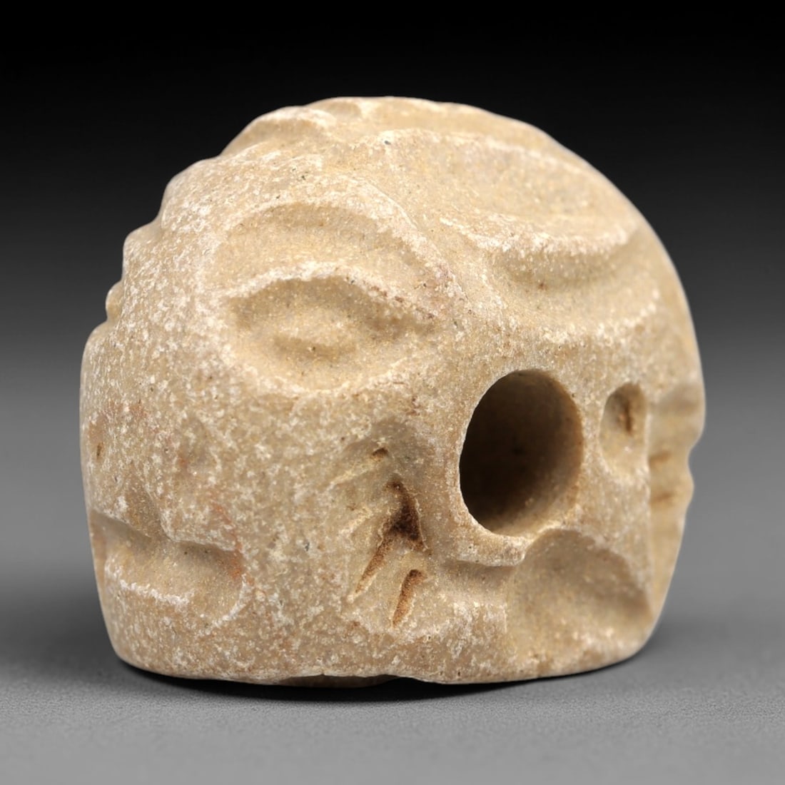 Ancient Stone Humanoid Stamp Seal - Near Eastern Ritual Artifact, 25AN: Carved from soft limestone, this stamp seal features a stylized humanoid head form with distinct facial features and a central perforation for suspension. The pale stone exhibits characteristic granul
