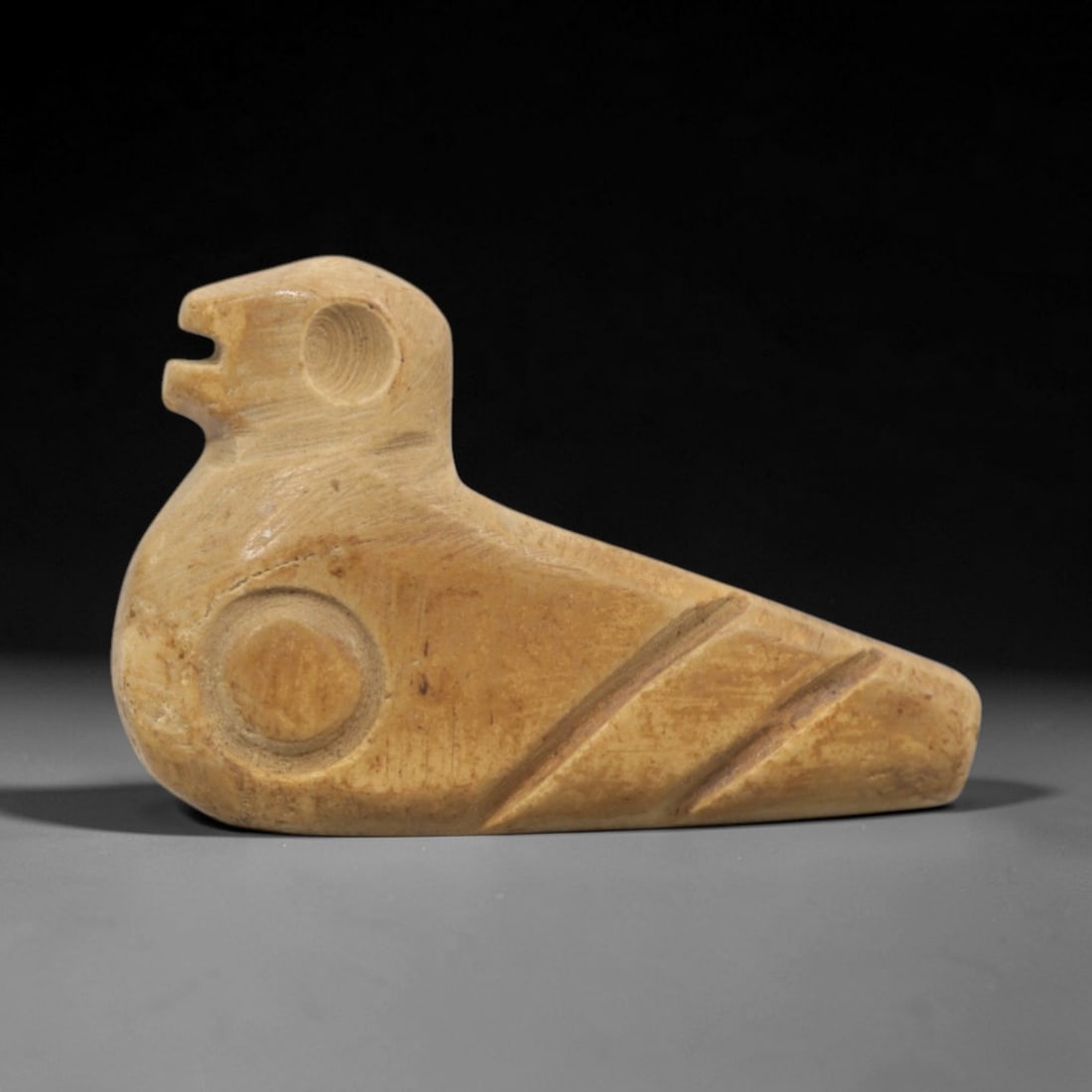 Ancient Limestone Bird Amulet - Near Eastern Animal Figure, 66ZW: This amulet is carved from pale beige limestone, depicting a stylized bird with a rounded head, open beak, and angular body. Incised details define the circular eye, a central chest motif, and two dia