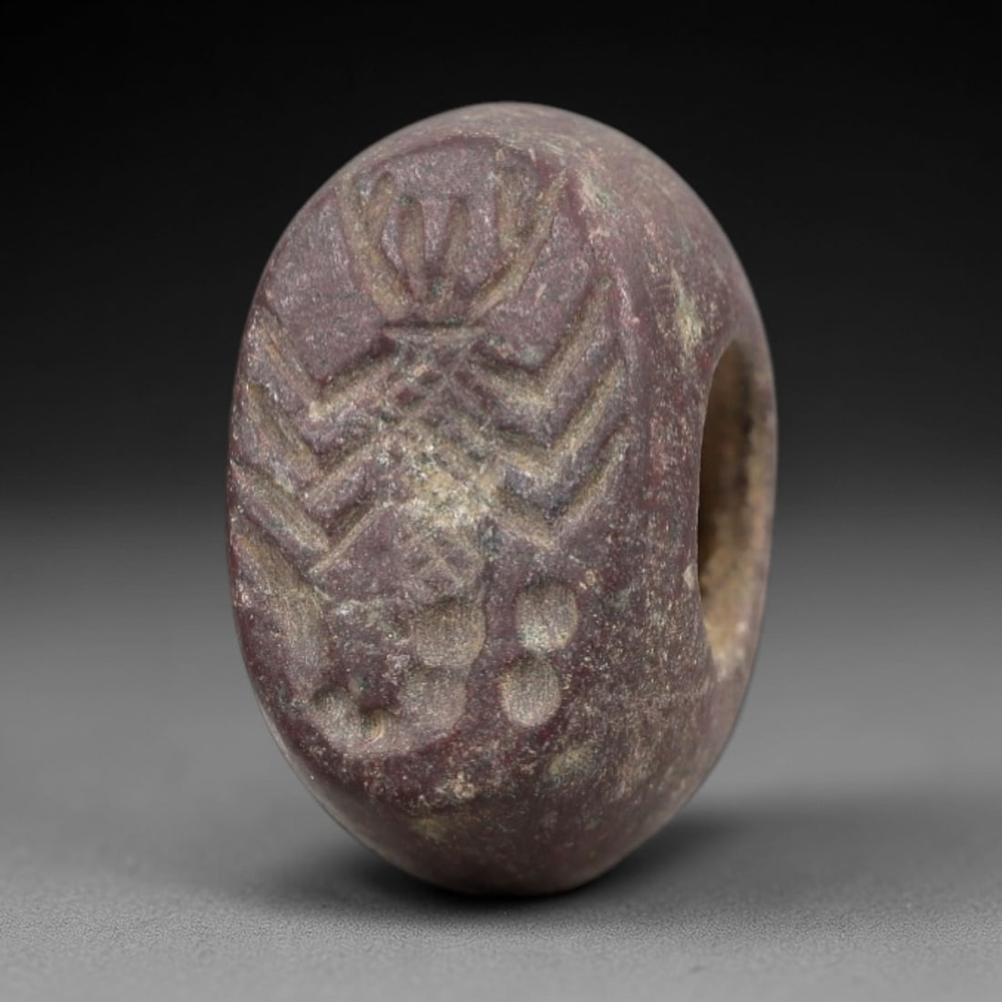 Ancient Stone Hemispherical Stamp Seal - Near Eastern Winged Figure, 6AN: Carved from a dense, dark reddish-brown stone, this hemispherical stamp seal features a flat, oval face incised with a standing winged anthropomorphic figure. The figure is depicted with a prominent h