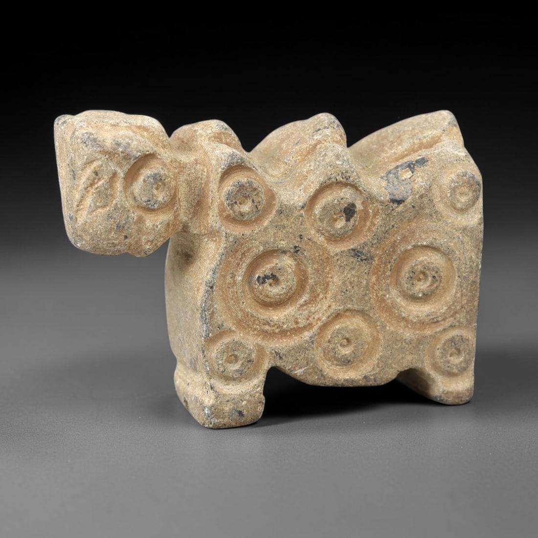 Ancient Stone Zoomorphic Figure - Near Eastern Idol, 65AM: This zoomorphic figure is carved from light stone, depicting a stylized quadrupedal animal form with a prominent head and a body adorned with concentric circular motifs in raised relief. The piece ref