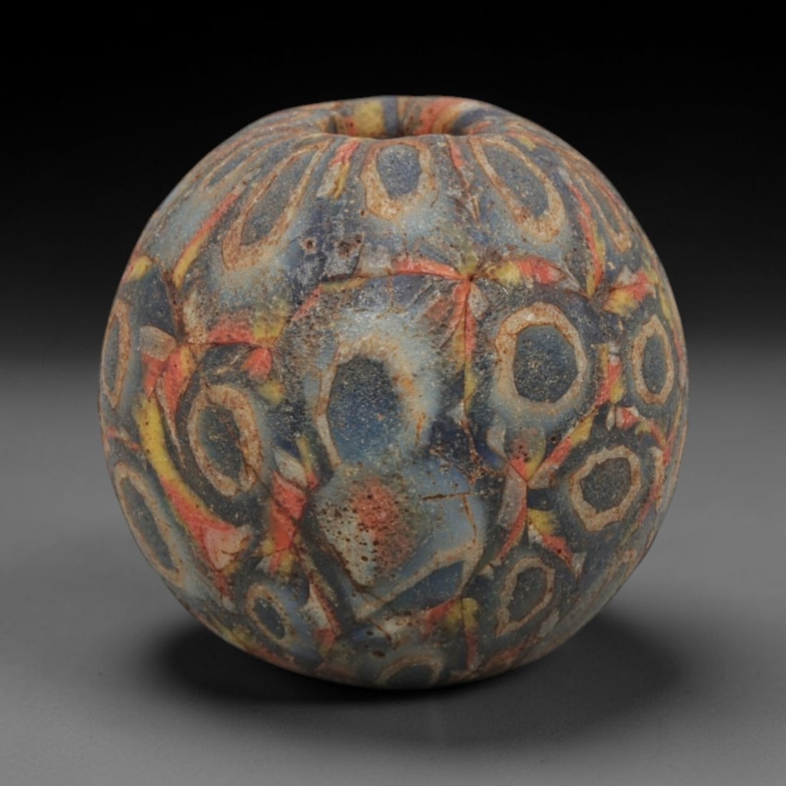 Ancient Glass Bead - Roman Egyptian Mosaic Amulet, 65ZN: Crafted from mosaic glass, this spherical bead features a central suspension hole and is decorated with intricate circular and floral motifs in blue, red, yellow, and cream glass inlay, characteristic