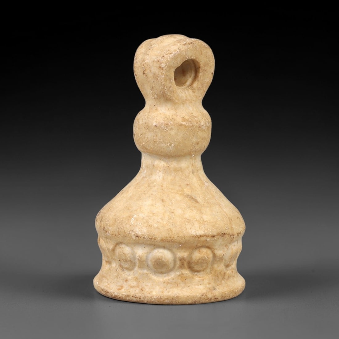 Ancient Stone Stamp Seal - Near Eastern Ritual Pendant, 95AL: This stamp seal is carved from pale beige stone with natural speckling and a weathered patina, featuring a tiered, bell-shaped form with a perforated suspension loop at the top. The lower edge is deco