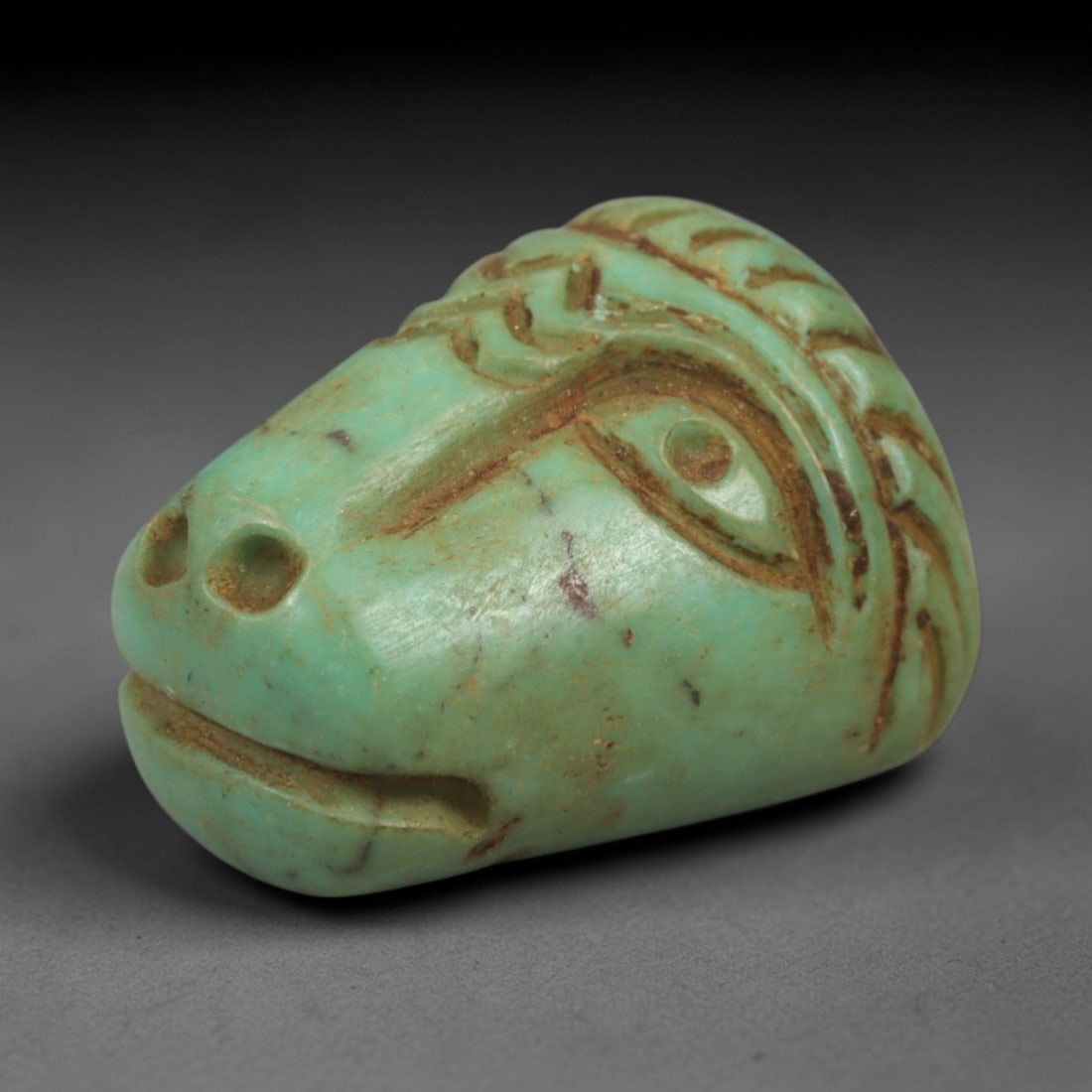 Ancient Turquoise Ram Head - Near Eastern Amulet Figurine, 75AK: Carved from polished turquoise, this miniature amulet depicts a stylized ram's head with incised linear details defining the eye, nostrils, mouth, and patterned mane. The form is compact and rounded,