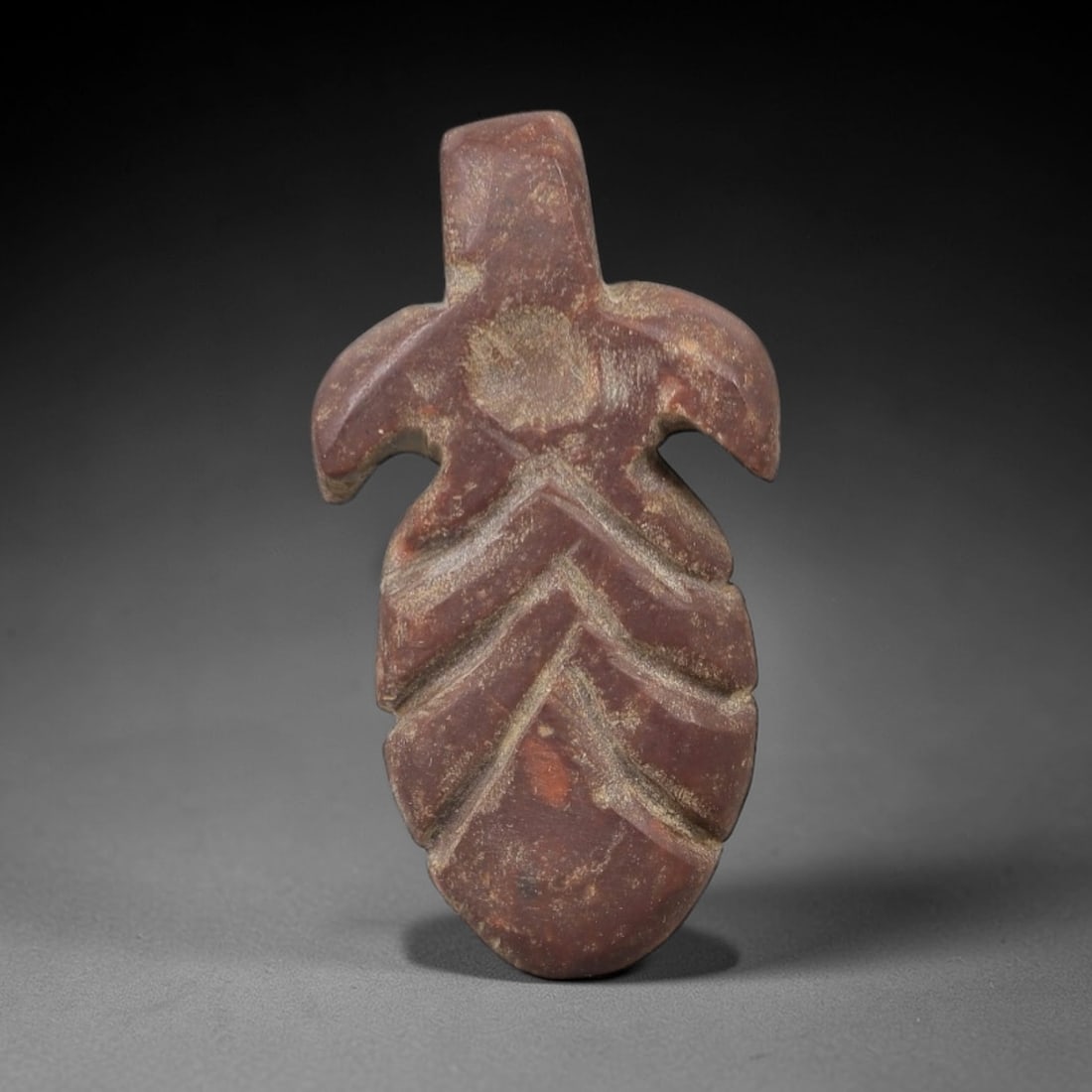 Ancient Stone Leaf Amulet - Near Eastern Ritual Figurine, 36AG: This amulet is carved from a single piece of deep reddish-brown stone, exhibiting a granular texture with pale ochre patina and subtle mineral inclusions across its surface. The form is stylized as a