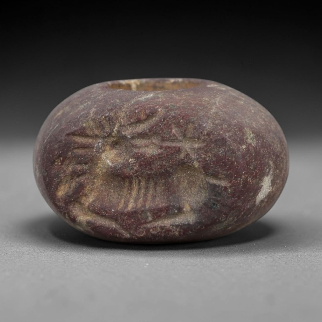 Ancient Stone Hemispherical Stamp Seal - Near Eastern Stag Figure, 90AN: Carved from a dense, dark reddish-brown stone, this hemispherical stamp seal features a flat, oval face incised with a stylized stag in profile. The stag is rendered with prominent antlers, linear det
