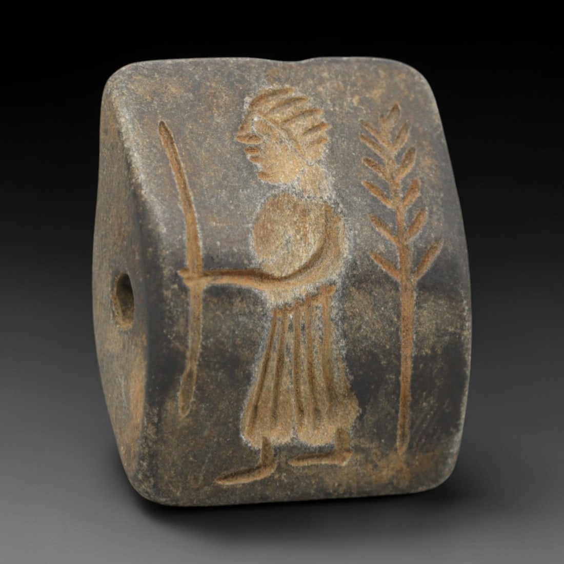 Ancient Schist Double Convex Bead Amulet - Near Eastern Figure with Tree Motif, 25ZS: Carved from dark gray schist, this 2.8x2.1cm double convex bead amulet features two distinct intaglio motifs: one side depicts a standing anthropomorphic figure in profile, holding a staff or weapon,