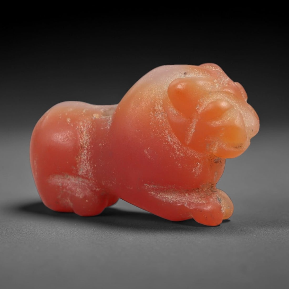 Ancient Carnelian Feline Amulet - Egyptian Figurine, 45XS: This amulet is carved from rich reddish-orange carnelian, depicting a stylized striding feline with rounded anatomical detailing and subtle incisions defining facial features and limb structure. A pie