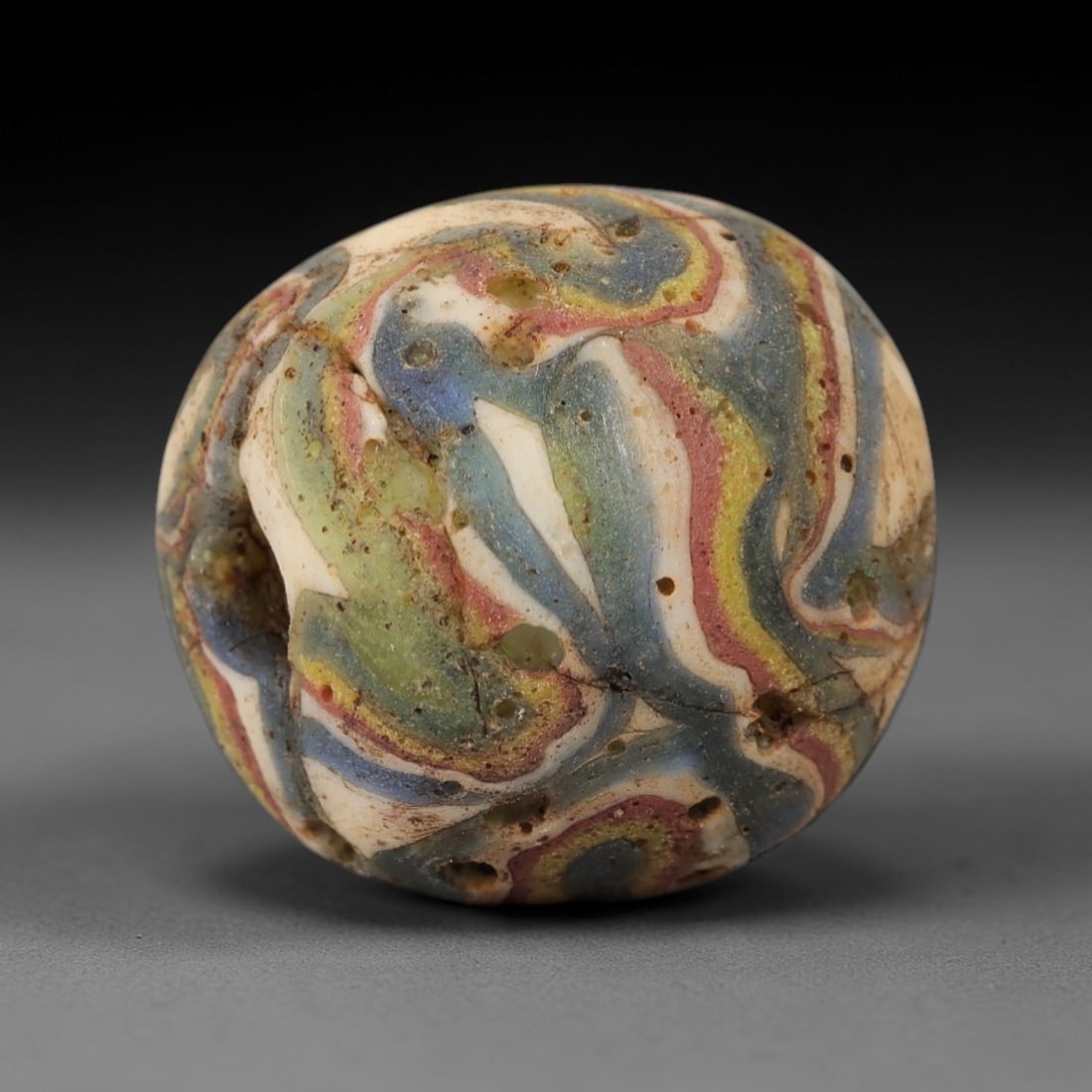 Ancient Glass Bead - Roman Swirl Bead, 45ZM: This ancient bead is crafted from polychrome glass, formed using the trailed and marbled decorative techniques characteristic of Roman glassworking traditions. The spherical form features a dynamic, s