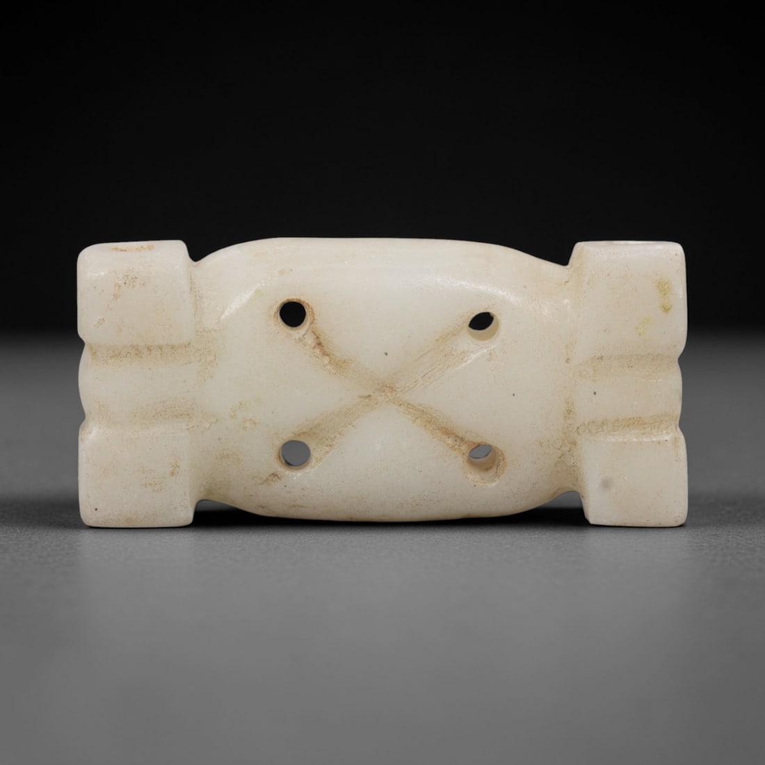 Ancient Marble Amulet - Near Eastern Ritual Relic, 98XR: Crafted from pale marble, this amulet features a compact, rectangular form with projecting lateral blocks at either end. The central face is marked by four circular suspension holes arranged in a cros