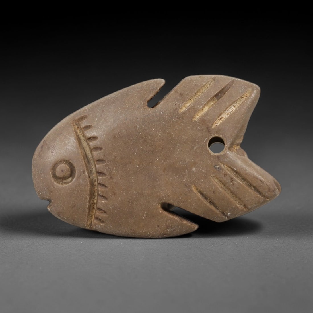 Ancient Egyptian Stone Amulet - Carved Fish Figurine, 98AE: Carved from beige stone, this amulet depicts a stylized fish with incised linear detailing, consistent with ancient Egyptian ritual amulets of the Late Period. The piece features a suspension hole at