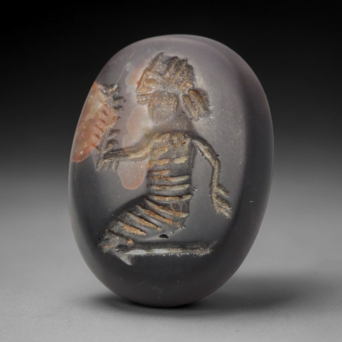 Ancient Agate Intaglio - Near Eastern Figural Motif, 32ZW: Carved from banded agate, this oval intaglio features a recessed depiction of a kneeling figural form, adorned with a stylized headdress and incised linear detailing to denote anatomical structure and