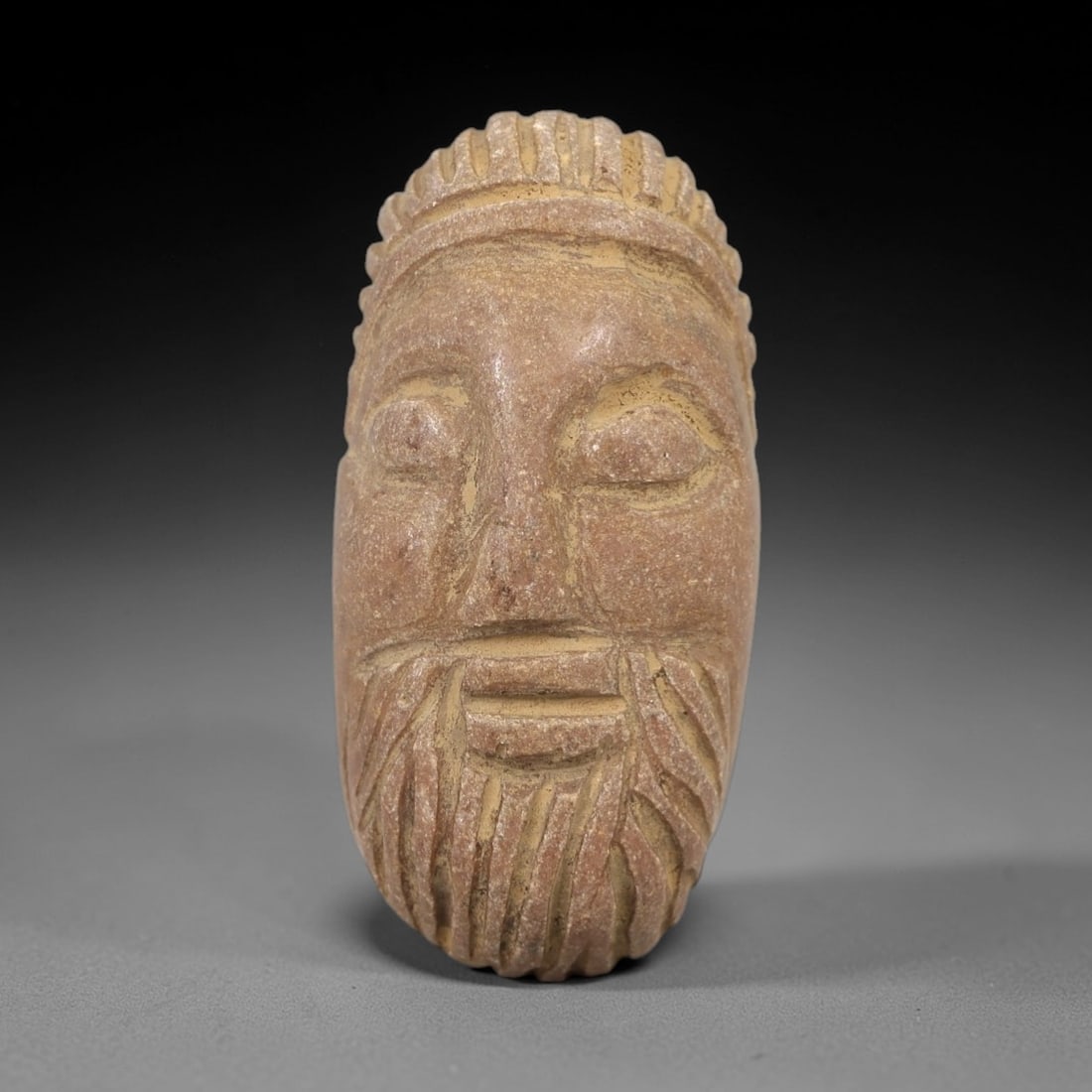 Ancient Stone Face Amulet - Near Eastern Relic, 11AM: This amulet is carved from a fine-grained tan stone, showcasing meticulous craftsmanship in the depiction of a human face. The form features closed, elongated eyes, a defined nose, and a stylized bear