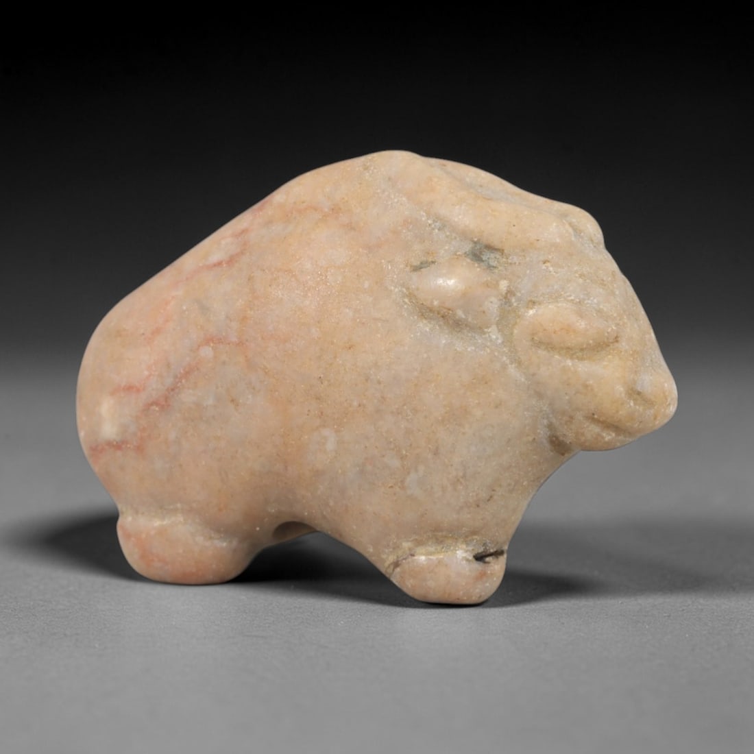 Ancient Stone Bovine - Near Eastern Animal Figurine, 81AR: This artifact is carved from a pale, pinkish-beige stone with subtle reddish veining, exhibiting a smooth, weathered patina and natural mineral inclusions. The form is a compact, stylized bovine, like